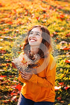 Curly young girl in yellow sweater on grass with autumn bouquet of dry leaves and flowers