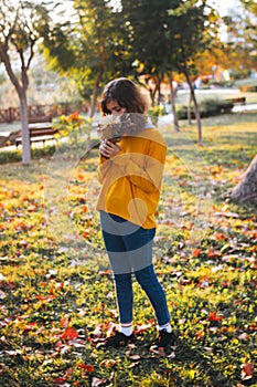 Curly young girl in yellow sweater on grass with autumn bouquet of dry leaves and flowers