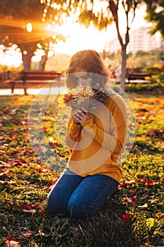 Curly young girl in yellow sweater on grass with autumn bouquet of dry leaves and flowers