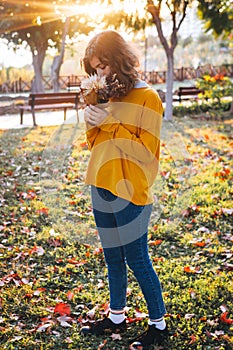 Curly young girl in yellow sweater on grass with autumn bouquet of dry leaves and flowers