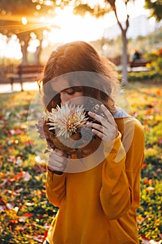 Curly young girl in yellow sweater on grass with autumn bouquet of dry leaves and flowers