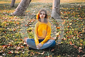 Curly young girl in yellow sweater and jeans sitting on fall grass with dry leaves. Autumn mood