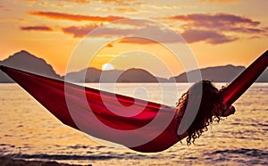 Curly young woman relaxing in a red hammock on a tropical island enjoying the sunset