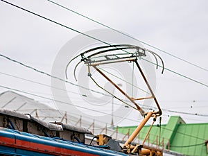 The current collector of the tram touches the copper high voltage metal power wires against the sky. The roofs of houses in the