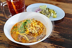 Curried noodle soup Khao soi with beef and spicy coconut milk on wood table.