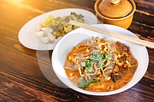 Curried noodle soup Khao soi with beef and spicy coconut milk on wood table.