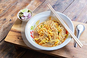 Curried noodle soup Khao soi with chicken meat and spicy coconut milk on wood table.