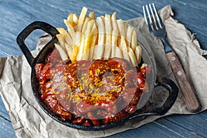Currywurst with french fries in black pan on craft paper.
