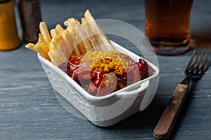 Currywurst with french fries in white bowl on wooden table.