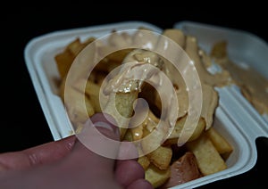 currywurst with fries into a cup on black background. traditional german food to go with dip at corona times, negative photo