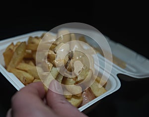 currywurst with fries into a cup on black background. traditional german food to go with dip at corona times, negative photo