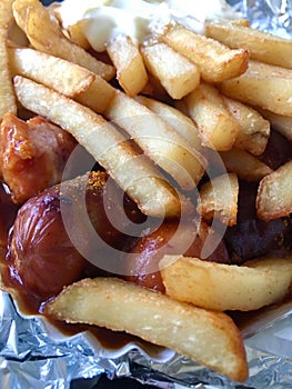 Currywurst & Pommes: Famous German Fast Food Curry Sausage with French Fries and Curry Sauce on aluminium foil