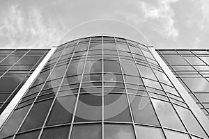 Curtain wall made of toned glass and steel constructions under sky. A fragment of a building. Black and white.