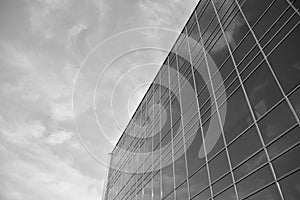 Curtain wall made of toned glass and steel constructions under sky. A fragment of a building. Black and white.