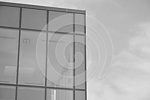 Curtain wall made of toned glass and steel constructions under sky. A fragment of a building. Black and white.