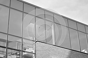 Curtain wall made of toned glass and steel constructions under sky. A fragment of a building. Black and white.
