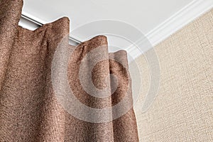 Curtains made of brown matting fabric hang on the ceiling cornice near the wall papered with a matting texture or rough
