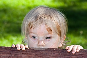 A curuos little boy hiding behind a bench