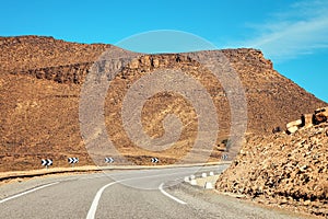 Curve on asphalt road , small Atlas mountains and low bushes both sides, clear sky above - typical landscape in Southern Morocco