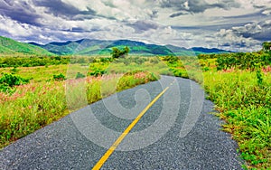 Curve line country road through the medow and mountain range with overcast sky