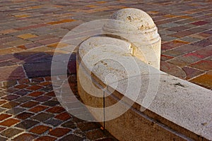 curved beige precast concrete curb and wheel chaser bollard with shadow. small brown cobblestone street pavement