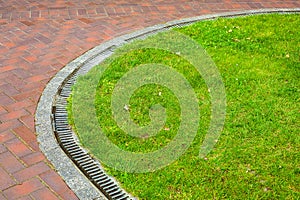 Curved iron grid drainage system in the park by the green lawn.