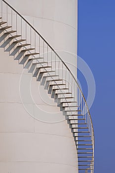 Curved line of spiral staircase on oil storage fuel tank with blue sky in vertical frame