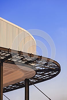 Curved metal awning structure with corrugated steel roof of modern building in construction site against blue sky