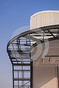 Curved metal awning structure with corrugated steel roof of modern building in construction site against blue sky