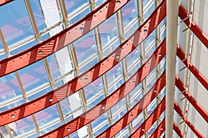 Curved red metal beams with perforation hold the window systems. Through the glass passes bright sunlight.Architectural