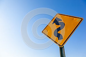 A curved road caution sign, blue sky with copy space