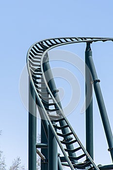 Curved Rollercoaster at a theme or amusement park empty green metal tracks and on blue sky background