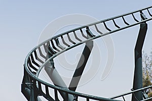 Curved Rollercoaster at a theme or amusement park empty green metal tracks and on blue sky background