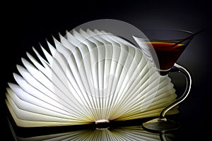 Curved stem martini cocktail glass and book with led lighting on dark background