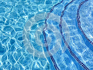 Curved steps into swimming pool, view from above through water on blue mosaic tiles. Distortion. Refraction