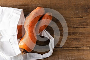 Curved ugly carrots in white eco bag on brown old wooden background with copy space. Vegetables with unusual strange