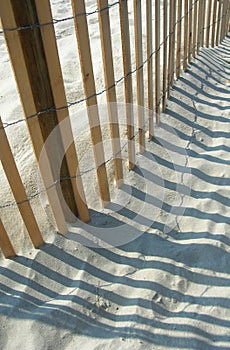 Curved wooden beach fence shadows on sand