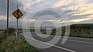 Curves ahead sign on open empty road in coastal landscape at sunset