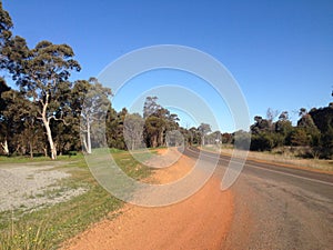Curving road with trees, sand and blue sky in Western Australia