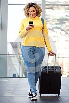 Curvy african american woman walking with suitcase and mobile phone