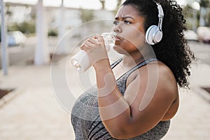 Curvy black woman drinking after jog routine outdoor at city park - Focus on face