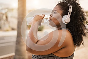 Curvy black woman drinking water after jog routine outdoor at city park - Focus on face