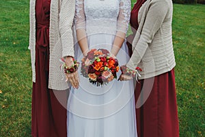 Curvy bride and bridesmaids are holding beautiful colorful bouquet with orange, red and pink peonies and roses. Wedding autumn