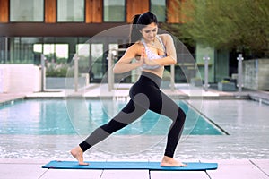 Curvy brunette female of mixed race ethnicity in active yoga pose at her luxury home by large swimming pool