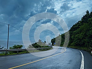 A curvy coastal moutain road after the rain with cloudy stormy cloud left is sea ocean right is the mountain