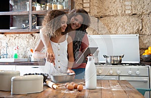 Curvy female foodie cooking with her daughter while looking at her recipe online on a tablet