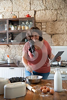 Curvy female foodie cooking while looking at her recipe online on a tablet