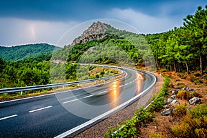 Curvy mountain road during storm with lightning striking in the distance