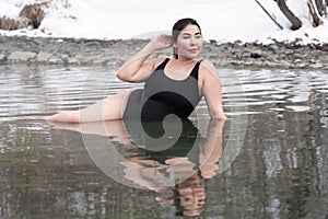 Curvy plus size young model in black bathing suit lying in geothermal water in outdoors pool at spa