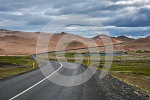 Curvy road, empty meadow and red mountains in the background in Myvatn region, overcast day in summe